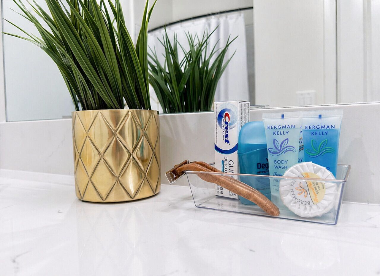 A bathroom counter with a gold decorative pot, a plant, and personal care items including body wash and deodorant.