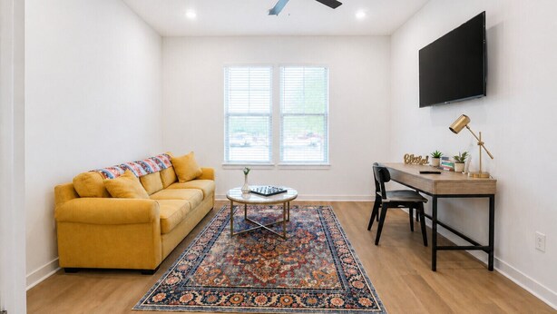 A living room with a sofa, coffee table, rug, TV, and desk with chair.