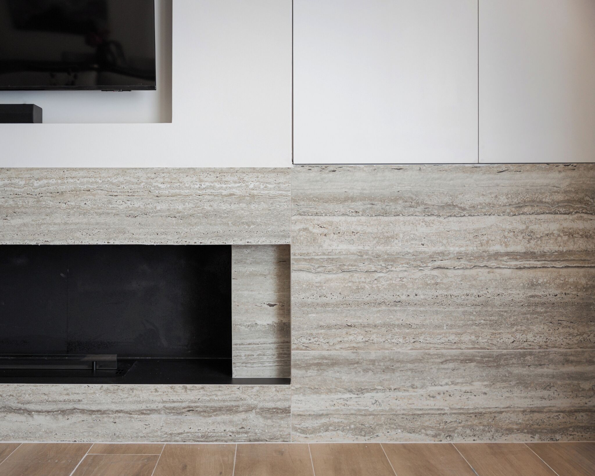 A modern interior with a built-in fireplace, white cabinetry, and a textured stone wall.