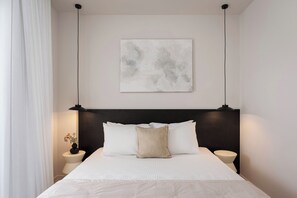A neatly made bed with white linens and two pillows, a black headboard, a wall-mounted abstract painting, and two bedside lamps. - Glyfada Prime Elegant Residence, Glyfada Prime Living (Glyfada)
