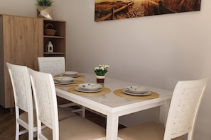 A dining table with white chairs, a small potted plant, and a painting on the wall. - Comfort Accommodation Baošići Montenegro-One Bedroom Apartment with Terrace and Sea View (2) (Baosici)