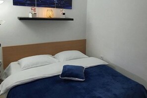 A bed with white bedding and a blue pillow, a wooden headboard, and a wall-mounted shelf with a lamp and decorative items. - Comfort Accommodation Baošići Montenegro-One Bedroom Apartment with Terrace and Sea View (2) (Baosici)