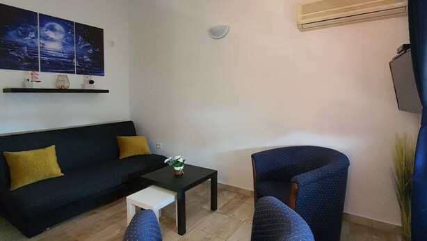 A living room with a black sofa, a small white table, a blue armchair, and a wall-mounted air conditioner. - Comfort Accommodation Baošići Montenegro-One Bedroom Apartment with Terrace and Sea View (2) (Baosici)