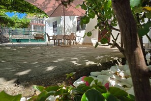 A patio area with a table and chairs, surrounded by greenery and white pebbles. - Comfort Accommodation Baošići Montenegro-One Bedroom Apartment with Terrace and Sea View (2) (Baosici)