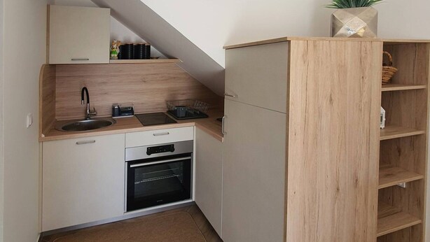 Pieni, käytännöllinen keittiö, jossa on pesuallas, liesi, uuni ja puinen kaappi.