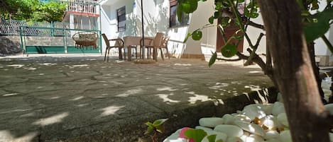 A patio area with a table and chairs, surrounded by a garden with white stones and green foliage.