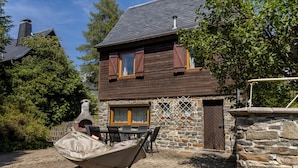 Una casa de fusta de dues plantes amb un mur de pedra i una xemeneu.