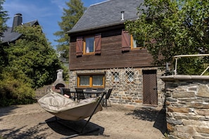 Une maison en bois à deux étages, dotée d’un mur en pierre et d’une cheminée.