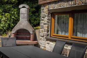 Un four extérieur en pierre, doté d’une cheminée, d’une fenêtre avec des rideaux et d’une table avec des chaises.