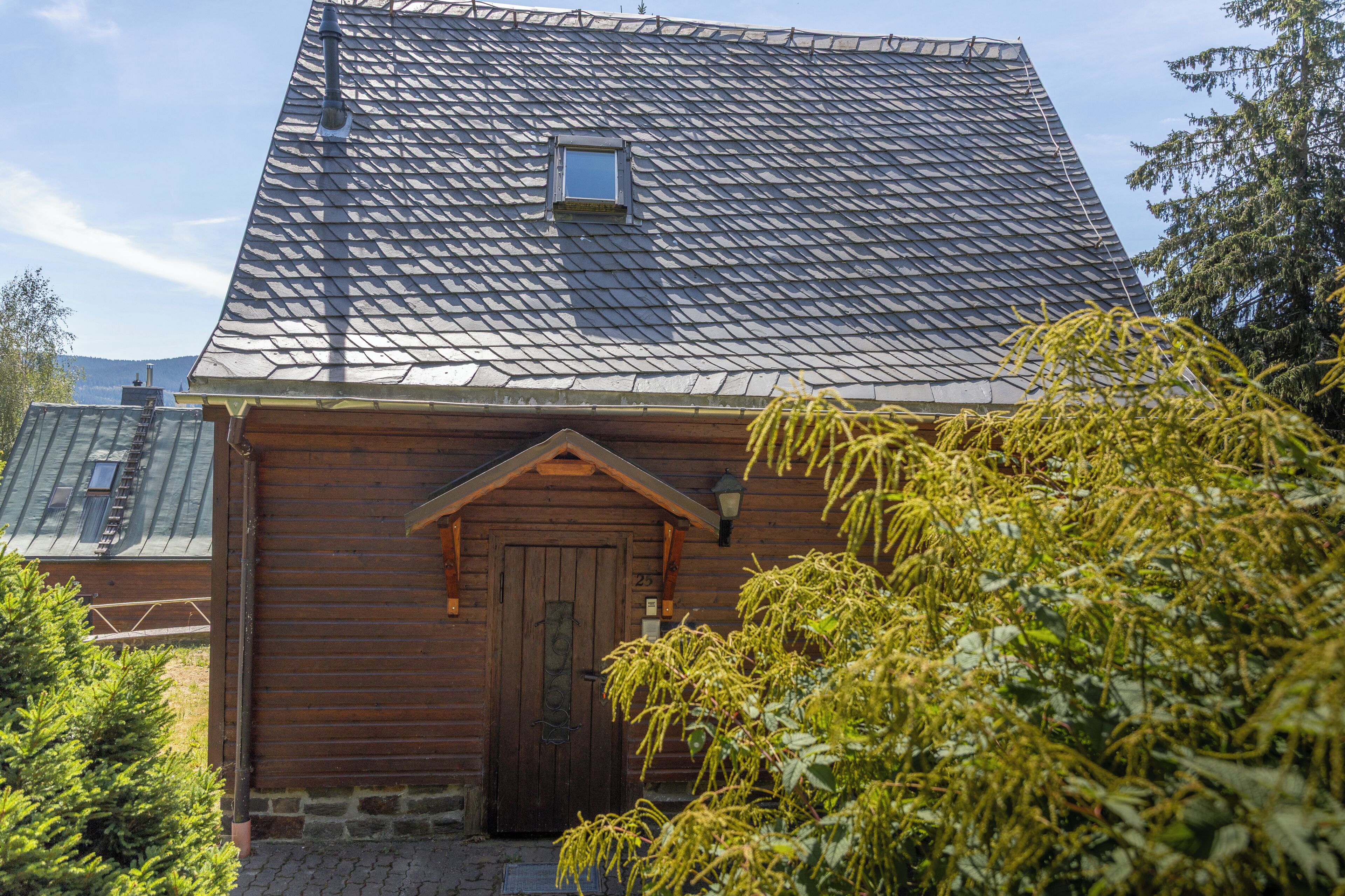 Ein Holzhaus mit einem steilen Satteldach, einem kleinen Fenster und einer Tür mit einer Hausnummer.