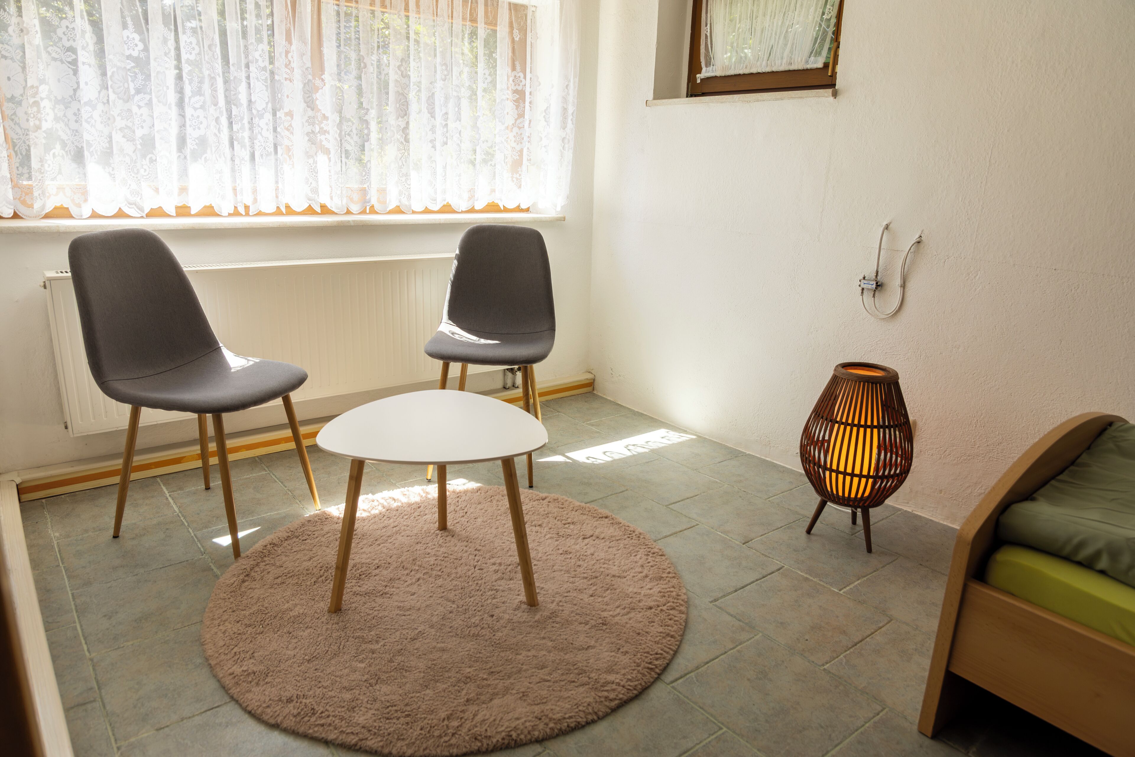 Ett rum med två stolar, ett litet bord, en golvlampa och en säng.
