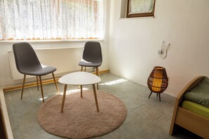 A room with two chairs, a small table, a floor lamp, and a bed.