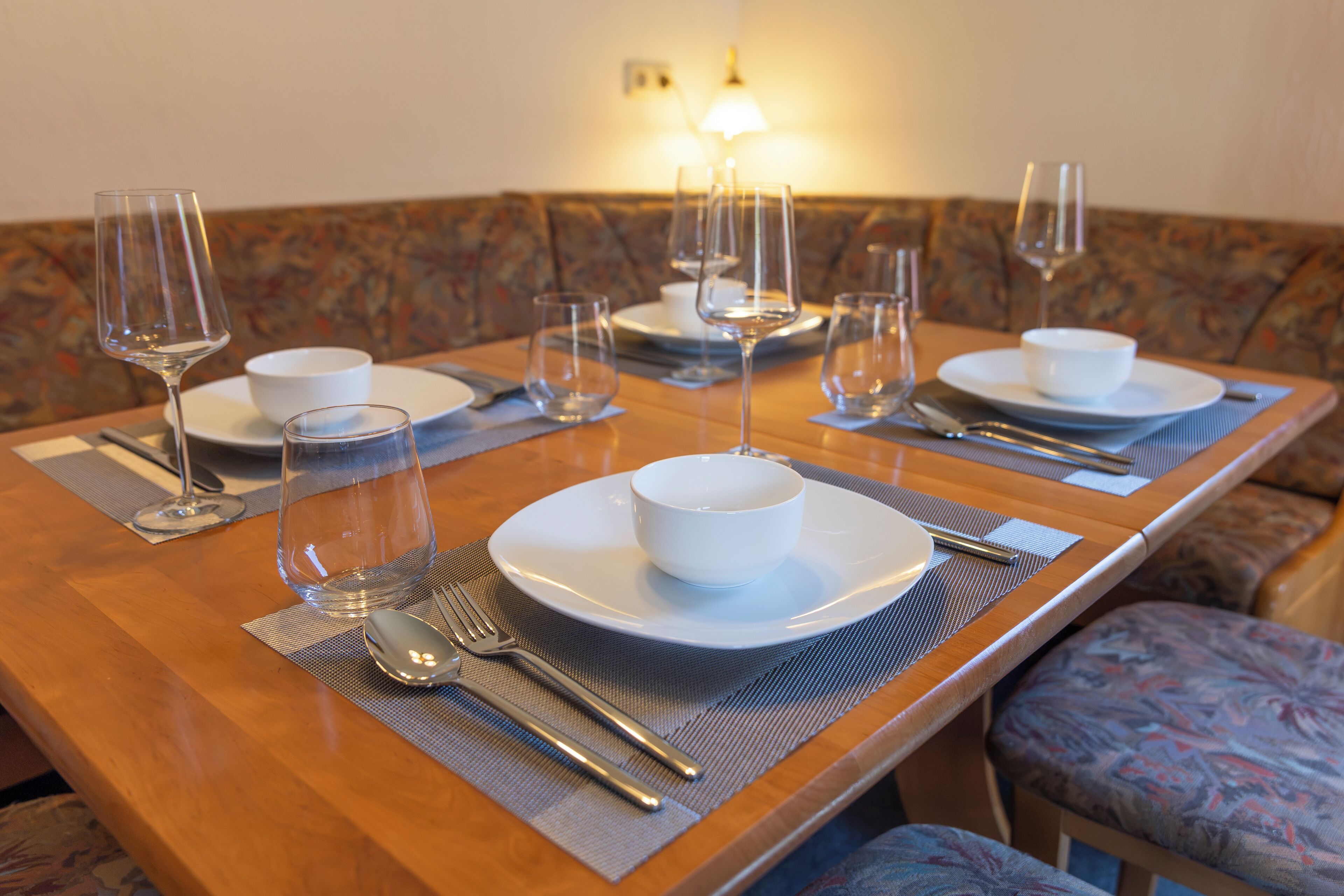 A dining table set with plates, bowls, cutlery, and wine glasses, indicating a prepared meal setting.