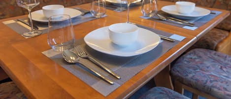 A dining table set with plates, bowls, cutlery, and wine glasses, indicating a prepared meal setting.