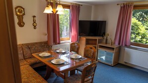A dining area with a table set for four, a sofa, a television, and a cabinet.