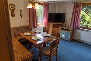 A dining area with a table set for four, a sofa, a television, and a cabinet.