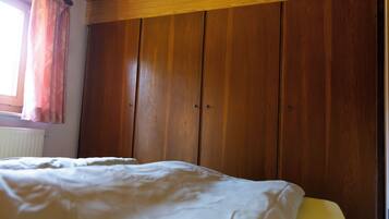 A bedroom with a bed, wooden wardrobe, and a window with curtains.