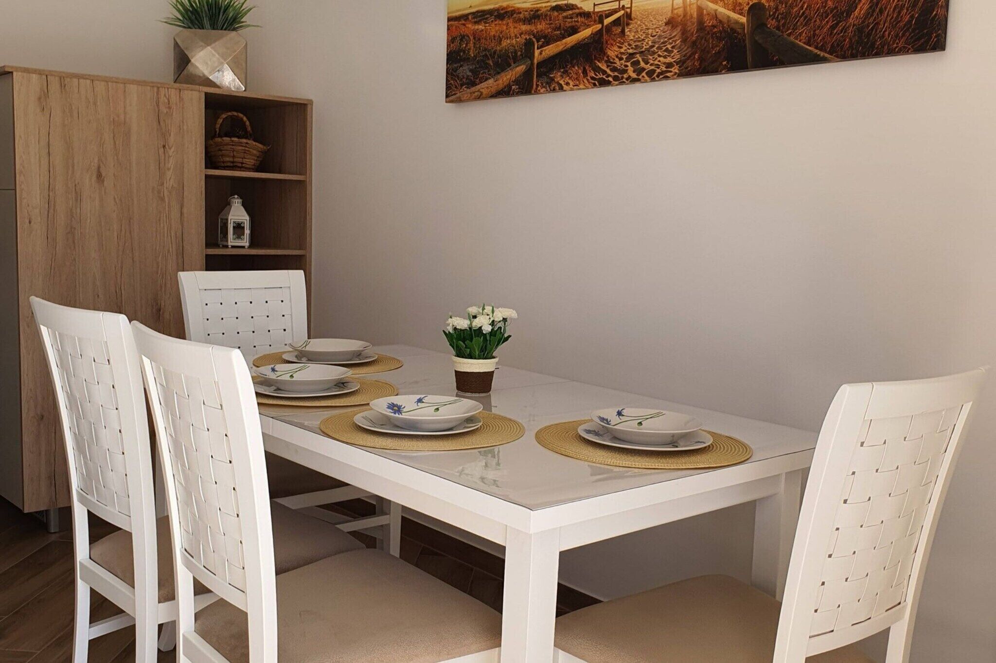 Une table à manger avec des chaises blanches, une petite plante en pot et un tableau accroché au mur.