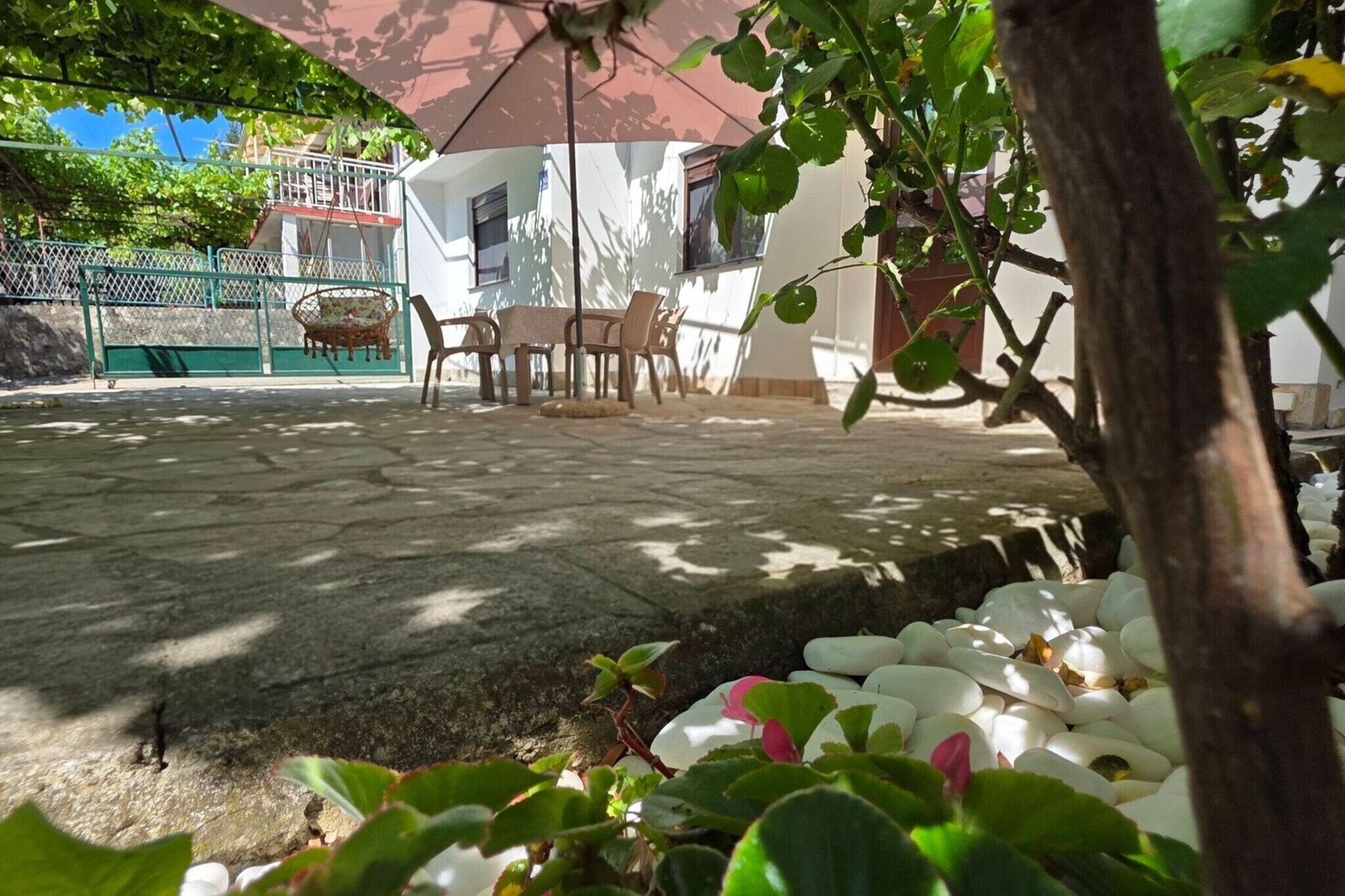 A patio area with a table and chairs, surrounded by greenery and white pebbles.