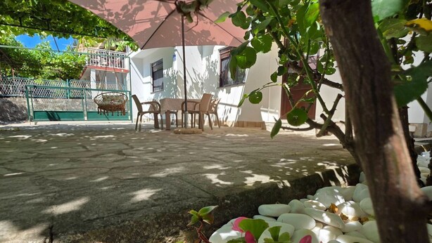A patio area with a table and chairs, surrounded by greenery and white pebbles. - Comfort Accommodation Baošići Montenegro-Double Room with Balcony and Sea View 2 (Baosici)
