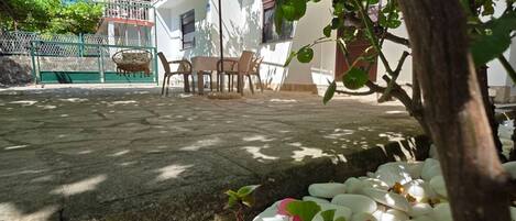 A patio area with a table and chairs, surrounded by a garden with white stones and green foliage.