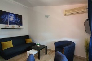 Ein Wohnzimmer mit einem schwarzen Sofa, einem kleinen weißen Tisch, einem blauen Sessel und einer Wand-Klimaanlage.