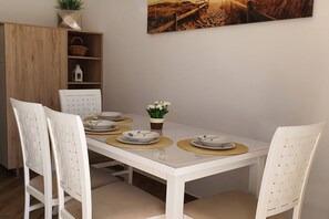 Ein Esstisch mit weißen Stühlen, einem kleinen Topfpflanzen und einem Gemälde an der Wand.