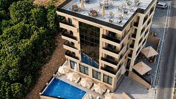 A multi-story hotel with a rooftop terrace, outdoor pool, and lounge area.