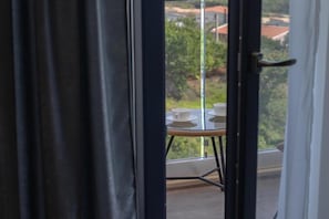 Un balcón con mesa y sillas, vistas a zonas verdes y edificios, y una puerta con cortina.