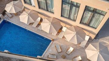 Une piscine entourée de chaises longues et de parasols, le tout bordé par un bâtiment doté de grandes fenêtres.