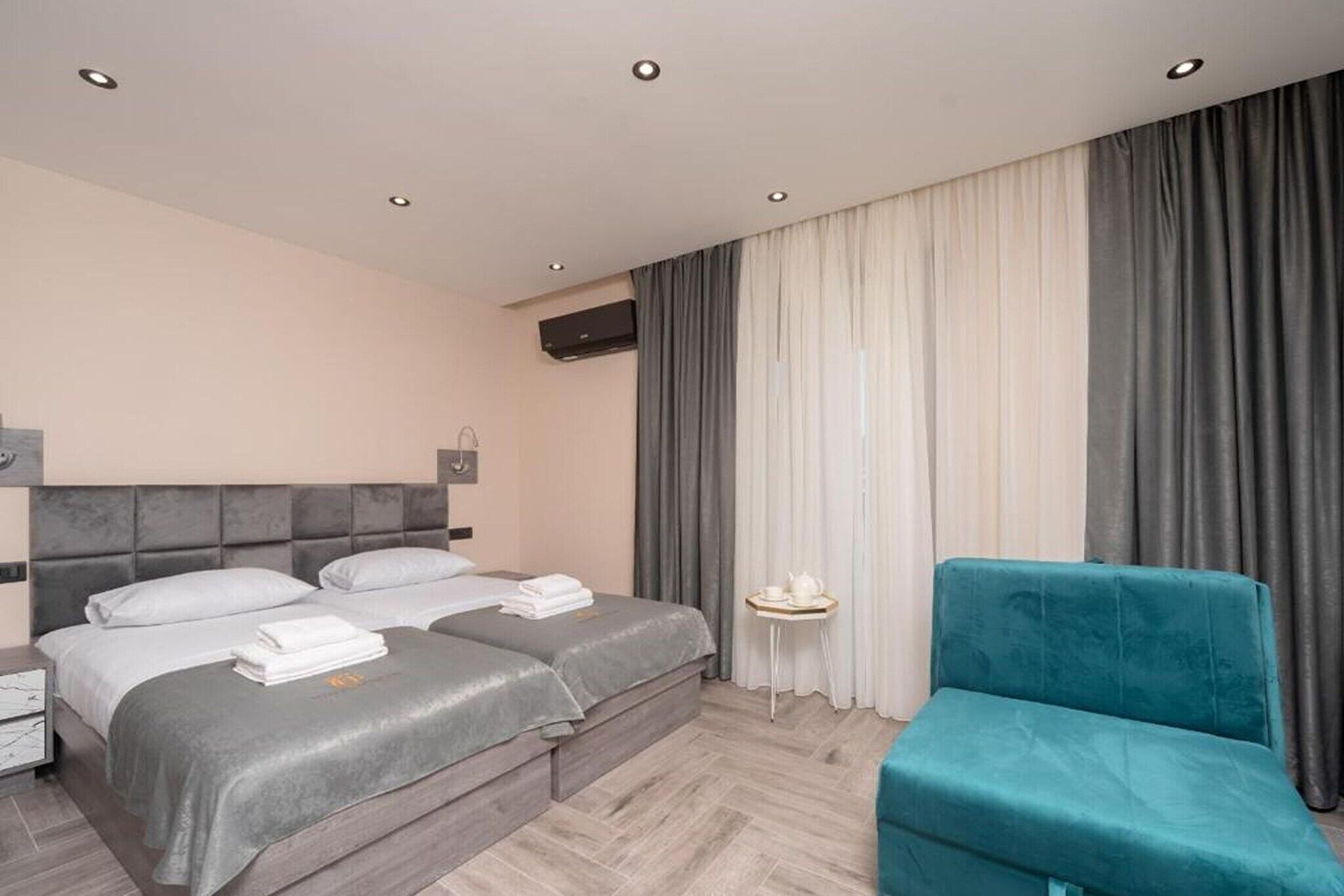 Ein Hotelzimmer mit zwei Betten, einem kleinen Tisch, einem blauen Stuhl und einem großen Fenster mit Vorhängen.