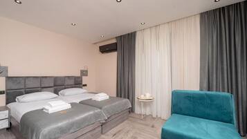 Ein Hotelzimmer mit zwei Betten, einem kleinen Tisch, einem blauen Stuhl und einem großen Fenster mit Vorhängen.