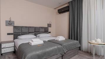 Ein modernes Hotelzimmer mit einem großen Bett, Nachttischen, einem kleinen Tisch mit Teekanne und einem Fenster mit Vorhängen.