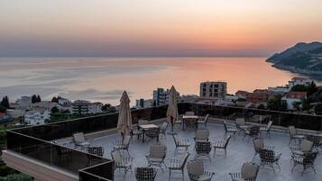 Eine Dachterrasse mit Sitzgelegenheiten im Freien und Blick auf das Meer bei Sonnenuntergang.