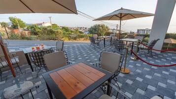 Eine Terrasse im Freien mit Tischen, Stühlen und Sonnenschirmen, mit Blick auf die Stadt.