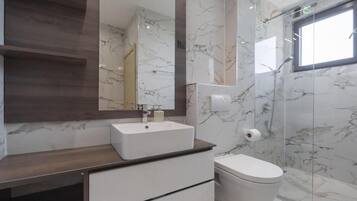 A modern bathroom with a marble wall, a large mirror, a white sink, and a toilet.