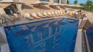A swimming pool with lounge chairs and umbrellas, surrounded by a building with large windows. - Hotel D'Iman - Classic Triple Room with Sea View and Balcony (202) (Dobra voda)