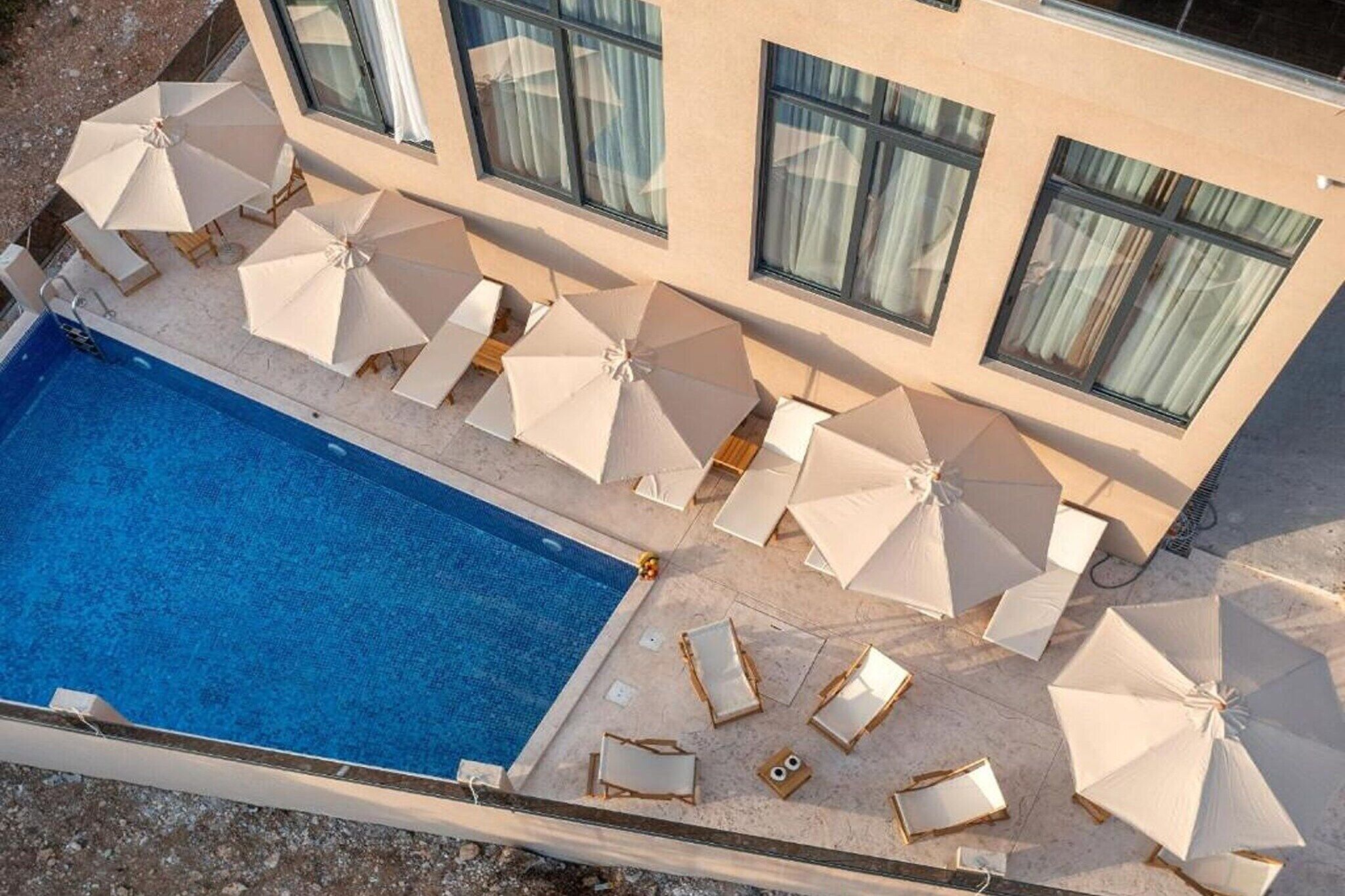 Ein Pool mit Liegestühlen und Sonnenschirmen, umgeben von einem Gebäude mit großen Fenstern.