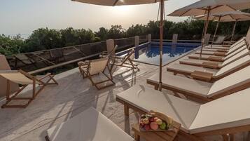 A rooftop pool area with sun loungers, umbrellas, and a table with fruit.