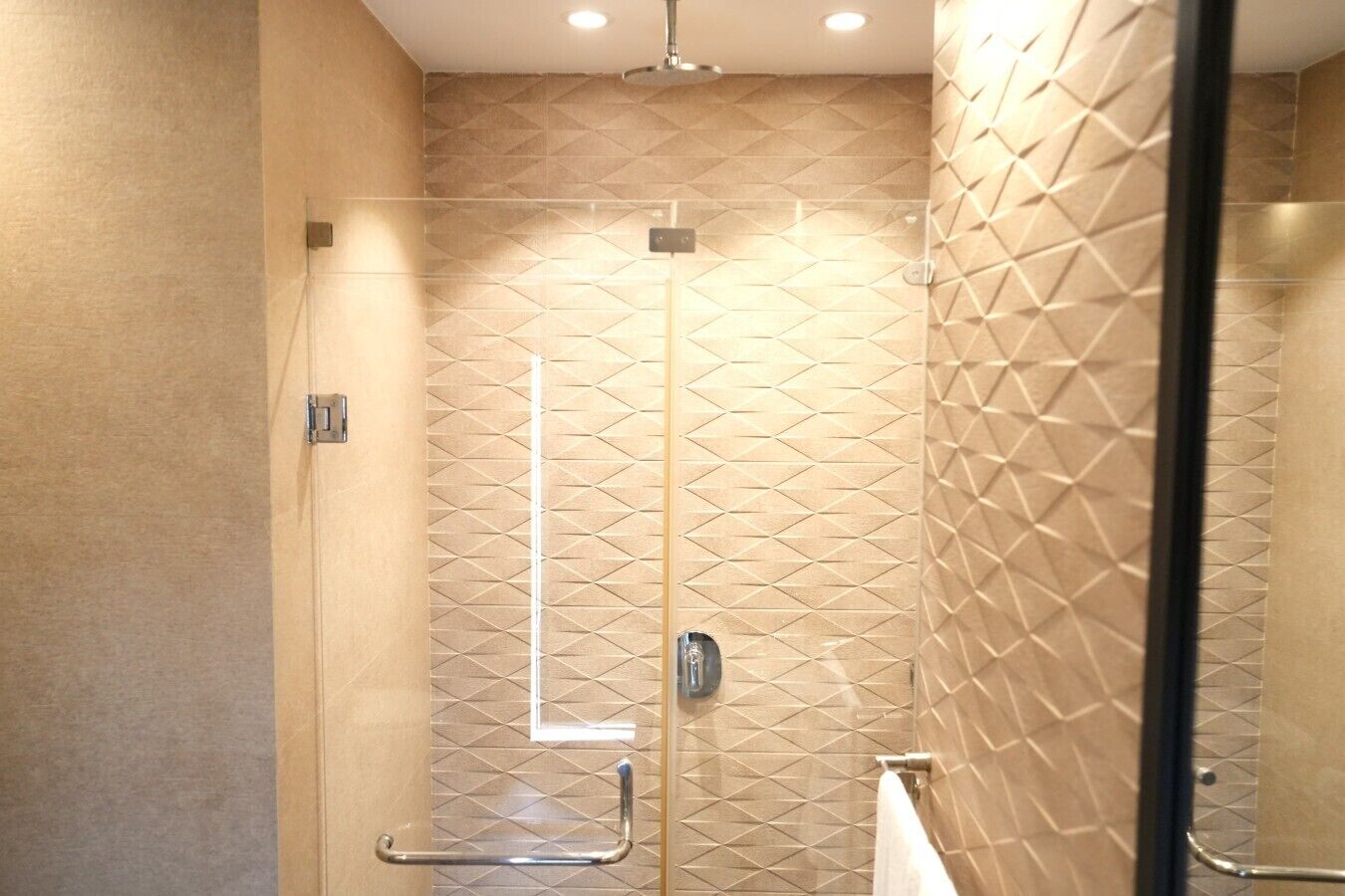 Eine moderne Dusche mit geometrischen Fliesenmustern, einer Glastür und einer Haltestange aus Metall.