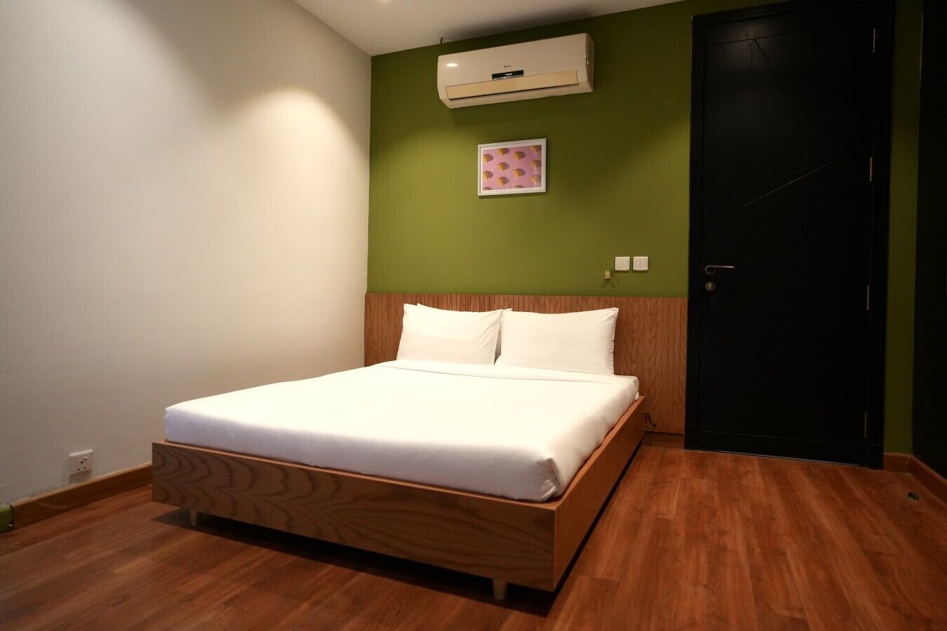 A hotel room with a wooden bed, green walls, a black door, and an air conditioning unit.