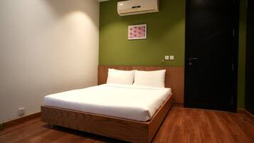 A hotel room with a wooden bed, green walls, a black door, and an air conditioning unit.