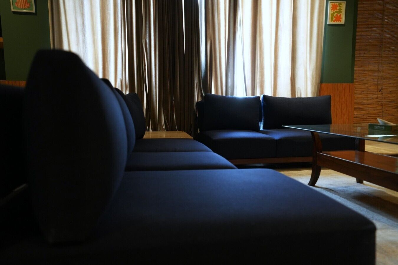 Un salon moderne avec un canapé d’angle, une table basse en verre et une vue sur l’extérieur à travers des rideaux transparents.
