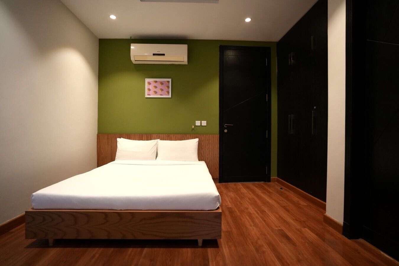 A bedroom with a bed, an air conditioner, a door, and a wall-mounted picture.