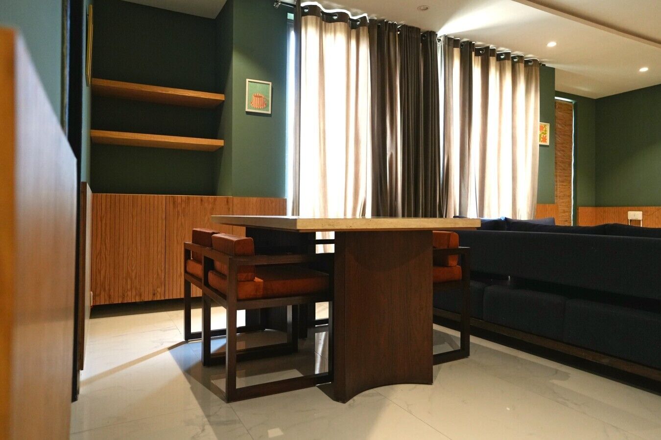 A dining area with a wooden table and chairs, a dark-colored sofa, and a window with curtains.