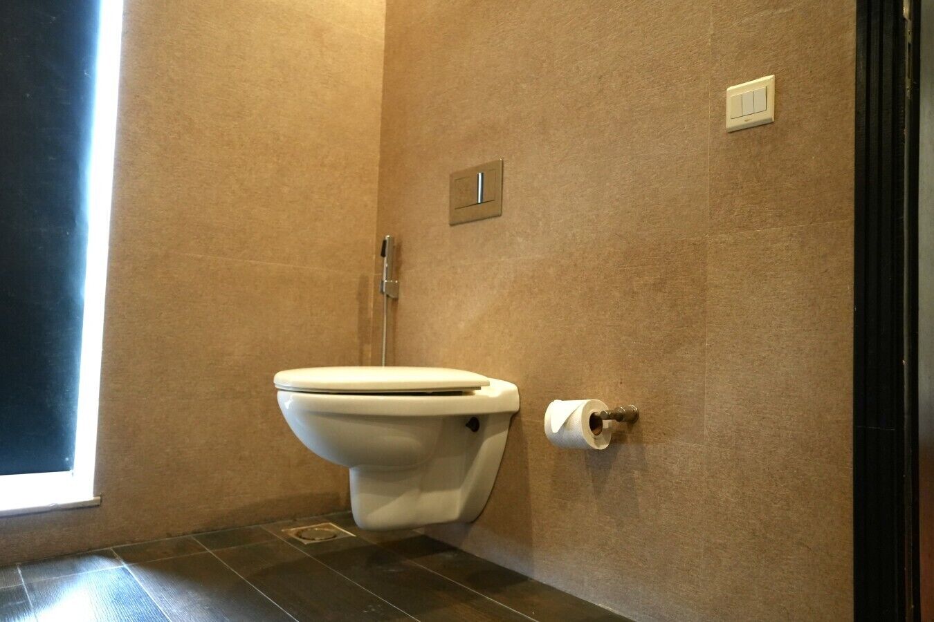 Une salle de bain équipée de toilettes, d’un distributeur d’essuie-tout et d’un interrupteur fixé au mur.