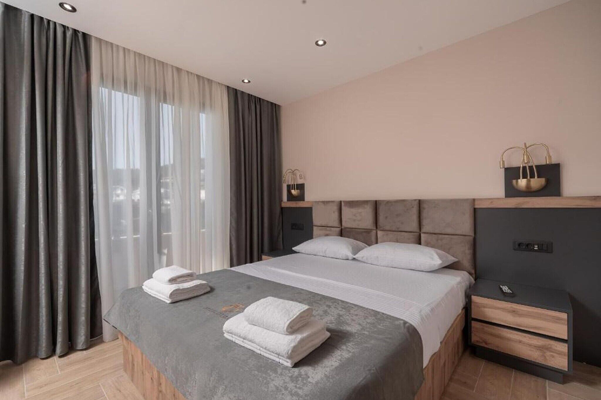 Ein modernes Hotelzimmer mit einem großen Bett, zwei Nachttischen, einer Kopfteil und einem Fenster mit Vorhängen.