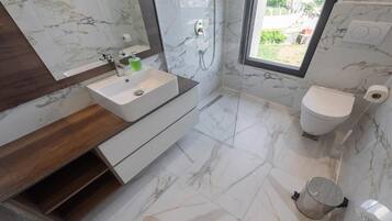 Ein Badezimmer mit Marmorboden, einem weißen Waschbecken mit Holztischplatte, einer Toilette und einem großen Fenster.