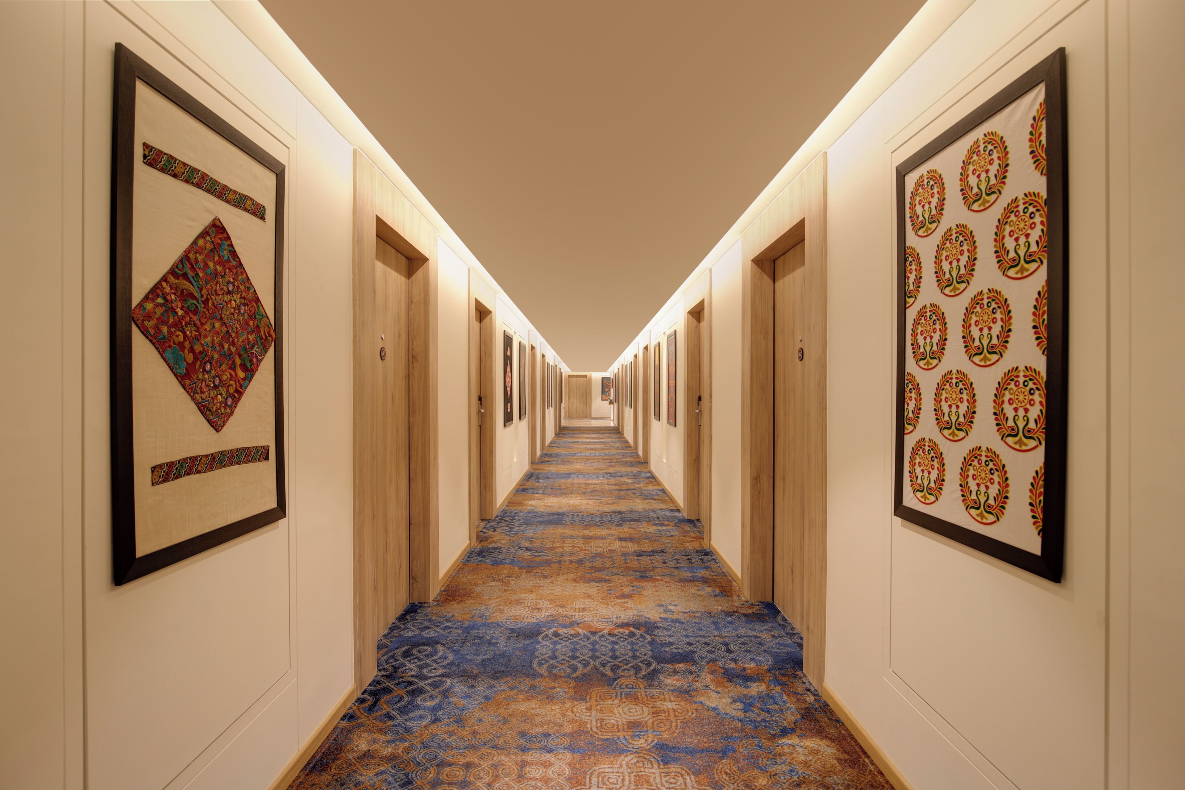 Pasillo de hotel con obras de arte enmarcadas en las paredes, alfombra estampada y puertas de madera.