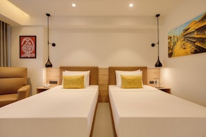 A hotel room with two beds, a nightstand with a phone, a lamp, and a painting on the wall. - Lemon Tree Premier Vadodara (Vadodara)